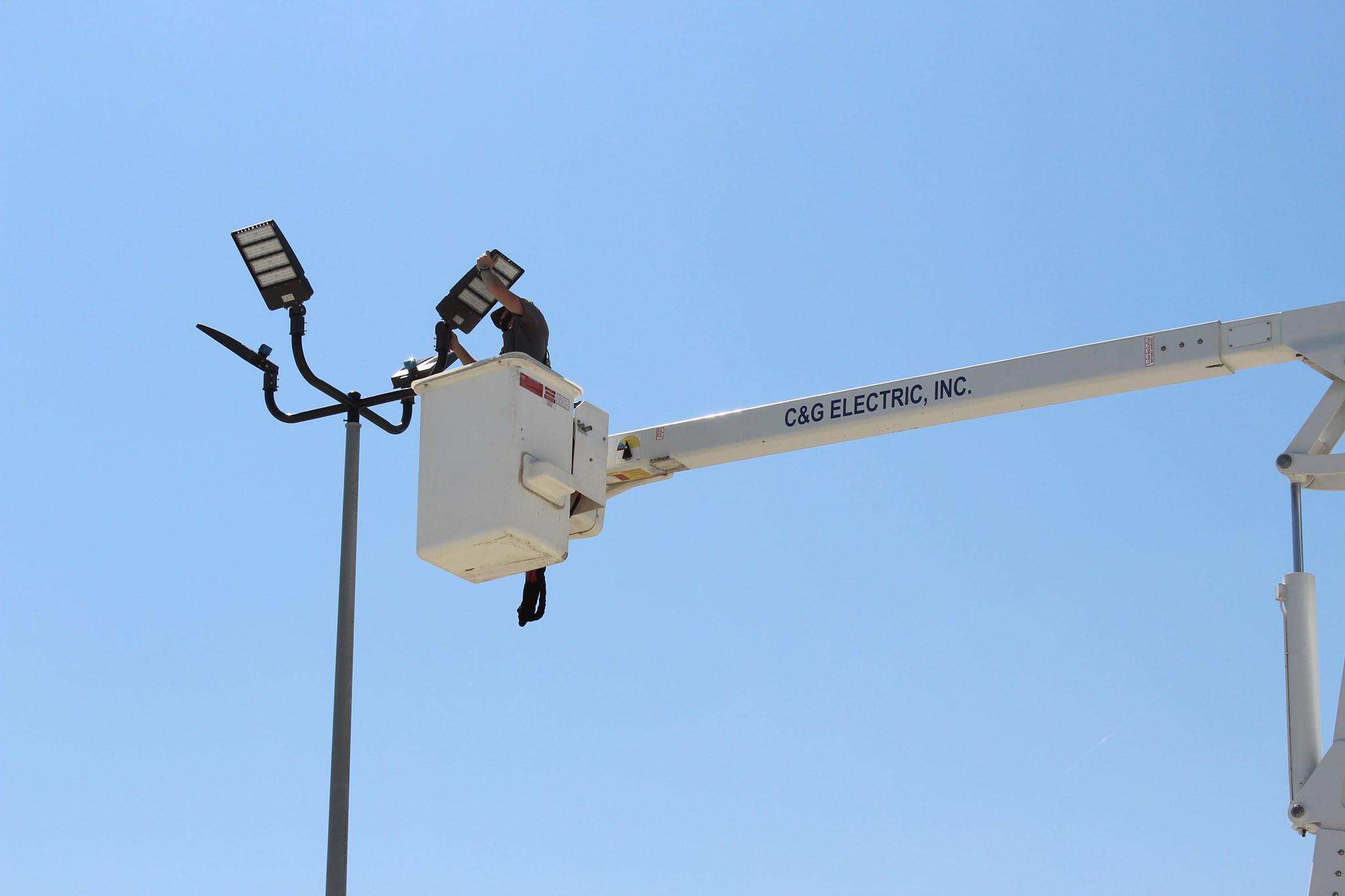 C&G Electric Inc electrician in bucket truck installing LED area lights — branded boom arm reads C&G Electric Inc, North Texas commercial lighting job