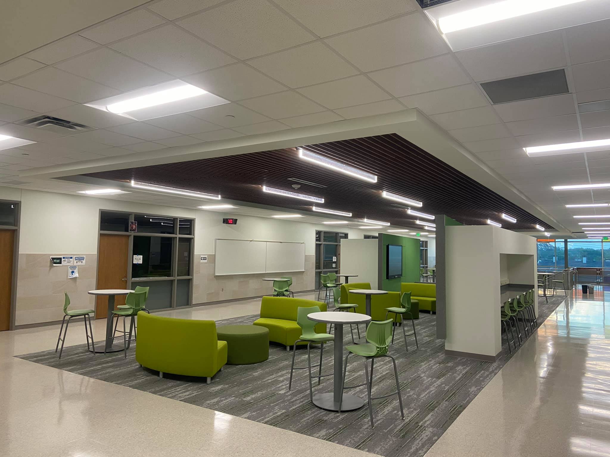 Completed commercial lighting project by C&G Electric Inc — modern school or office common area in North Texas with linear LED ceiling fixtures, clean tile floor, and green furnishings