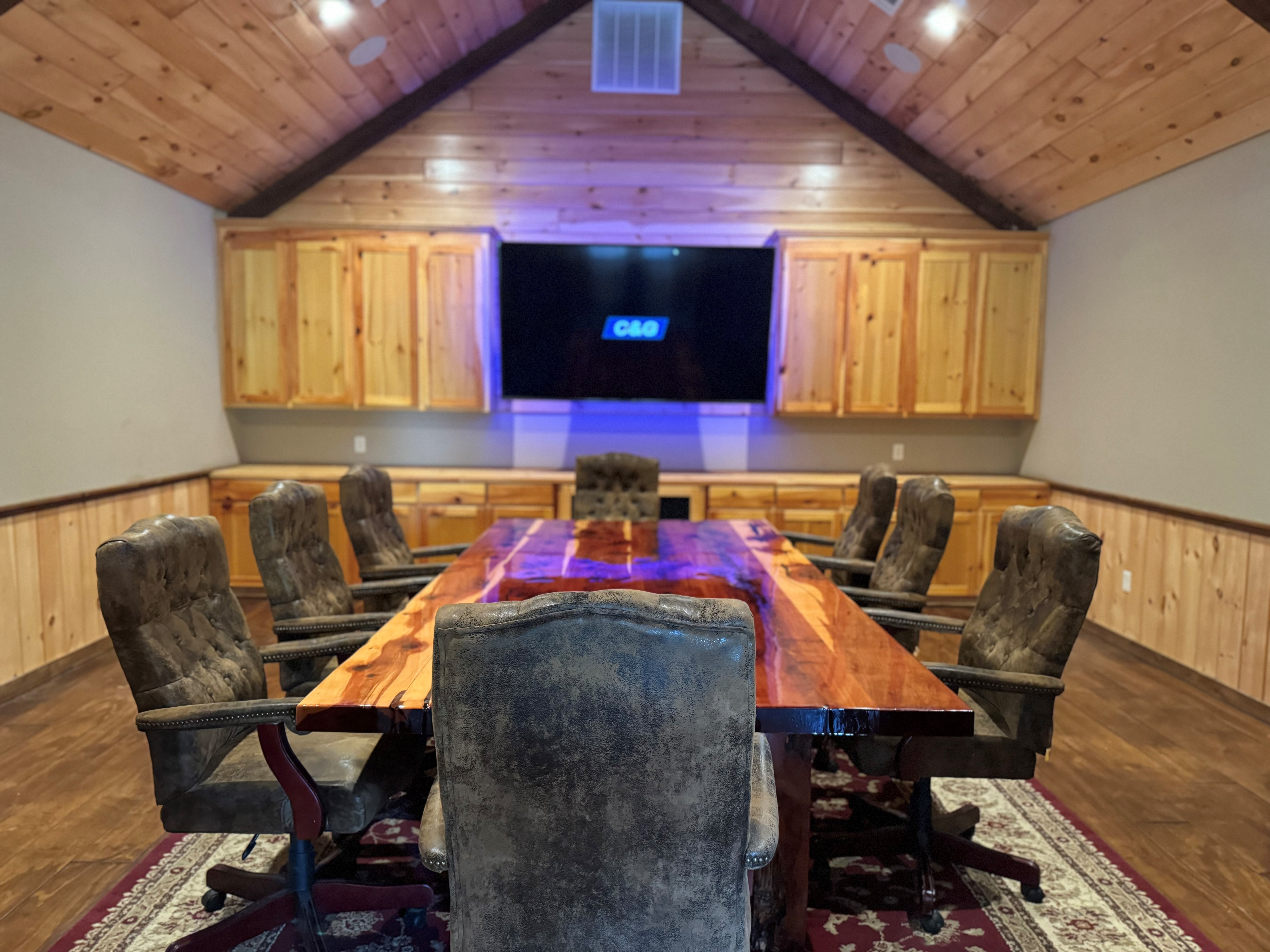 C&G Electric Inc conference room at the Krum, TX office — vaulted cedar ceiling, live-edge cedar table with leather chairs, knotty pine cabinetry, and C&G logo displayed on large screen