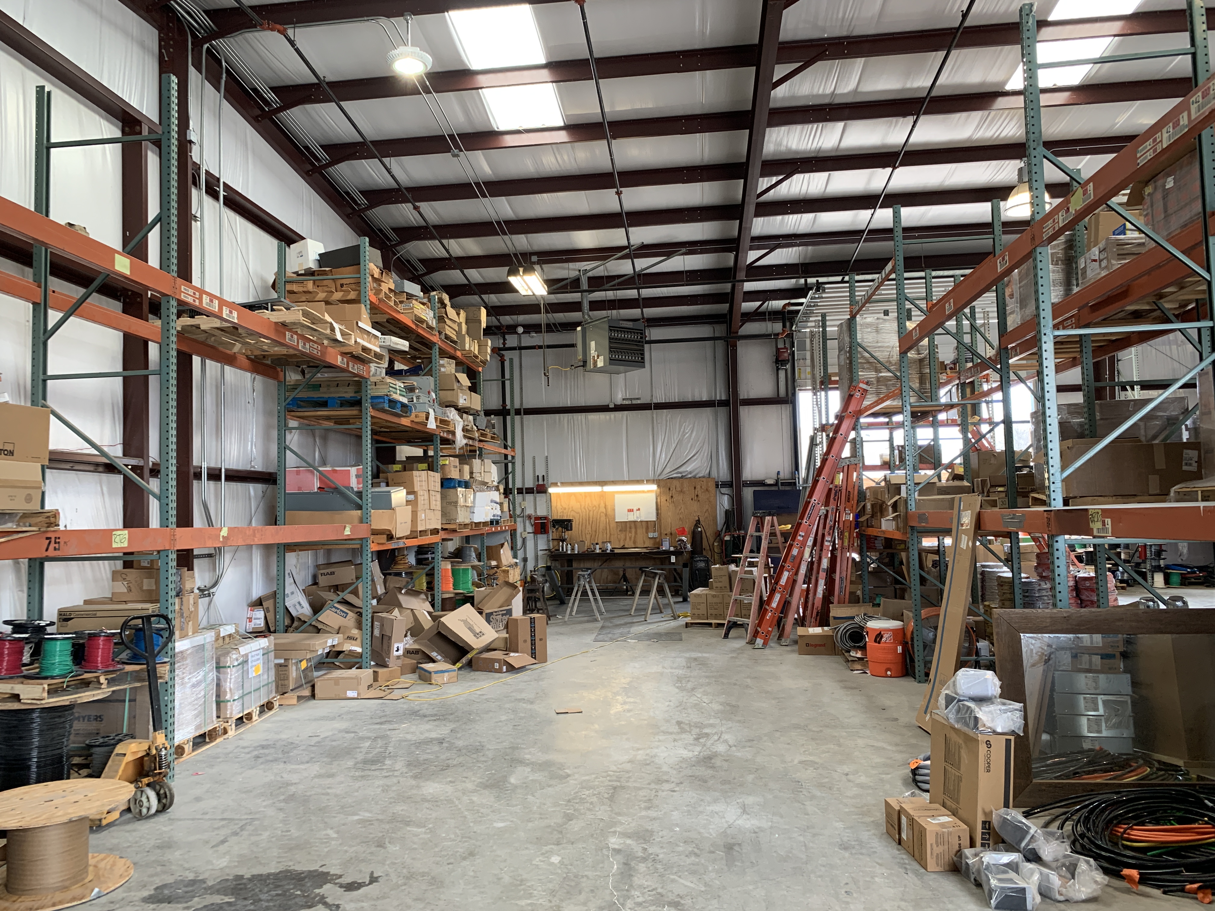 C&G Electric Inc supply warehouse in Krum, TX — team member in orange pulling materials from fully stocked shelves of wire, panels, conduit, and electrical supplies